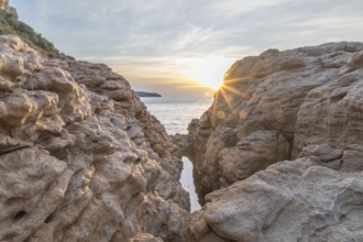 Stunning view of the sun setting over the Mediterranean Sea, seen between rocky formations on the