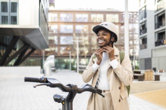 A cheerful black woman secures her helmet while standing next to a bicycle in the city The scene