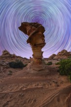 A mesmerizing view of swirling star trails in the night sky above a unique rock formation in a