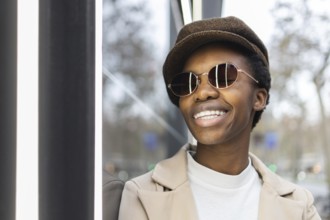 A fashionable black woman wearing sunglasses and a hat, smiling confidently in an urban setting Her