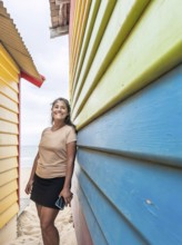 A smiling woman leans against the colorful Brighton Bathing Boxes in Melbourne, Australia. The