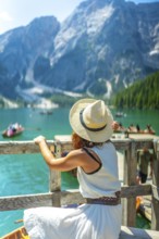 Woman wearing straw hat admiring scenic landscape of lake braies with boats and turquoise water in
