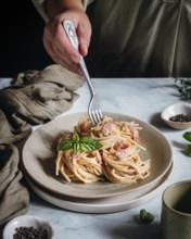 A hand elegantly twirls a fork in a creamy pasta dish topped with fresh basil leaves. The scene