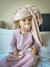Child in pyjamas with dummy and scarf, lovingly and playfully depicted