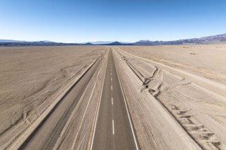 A straight road stretches across a vast desert landscape of the argentine Puna, leading into