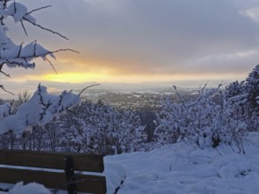 Snowy bench at an orange sunset with a view of Kronach, Frankenwald nature park Park