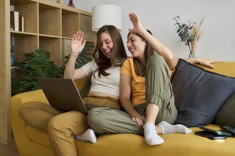 A cheerful lesbian couple relaxes on a cozy yellow sofa, smiling and enjoying quality time together