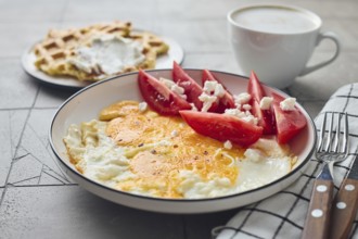 From above a delicious homemade breakfast featuring fried eggs with feta cheese and fresh tomato