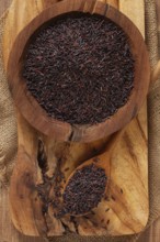 Natural black rice in a wooden bowl and spoon on a wooden surface in rustic style, top view