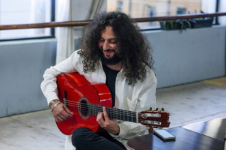 Latin man with long hair playing red bass guitar in studio