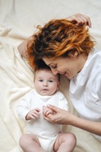 A mother shares a tender moment with her newborn baby girl, lying on a soft, cream-colored blanket.