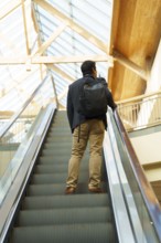 Young Chilean businessman in smart attire with a backpack ascends an escalator in a modern,