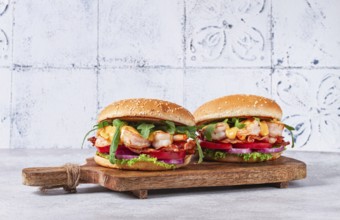 Two shrimp burgers and buns with sesame seeds, bacon, lettuce, tomatoes and onions, On a wooden