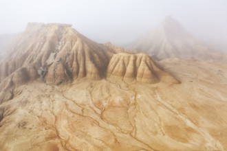 Aerial view of rugged desert formations enveloped in mist Erosion patterns are visible on the sandy