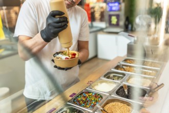 Barista wearing black gloves preparing a customized acai bowl, adding a creamy sauce over fresh