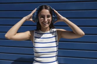 A young woman wearing headphones smiles joyfully while enjoying music in the city outdoors. She