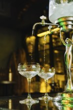 Elegant setup with absinthe fountain, gently dripping ice water into vintage crystal glasses. The