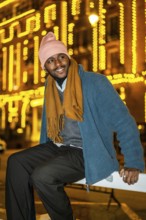 Vertical portrait of an african man sitting outdoors in a Christmas night in the city