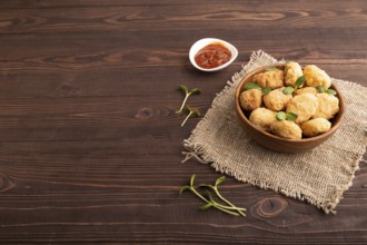 Fried crispy Chicken Nuggets with ketchup, microgreen on brown wooden background and linen textile.