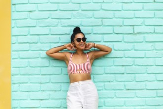 A young Latin woman stands against a vibrant turquoise wall in Mancora, Peru. Wearing a striped top