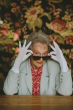 Elegant elderly woman posing confidently, wearing white gloves and sunglasses. Her stylish outfit