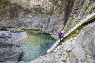 A canyoneer rappels down steep cliffs next to a waterfall, surrounded by breathtaking natural