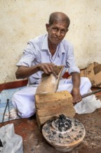 Elderly man works with bricks and coal in traditional clothes, a man burns sapphires in a small