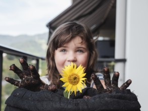 A smiling young girl shows off a bright sunflower and her dirty hands after gardening, capturing a