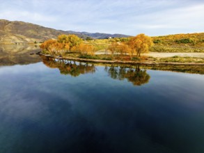 Aerial view of a tranquil lake in Queenstown during autumn, showcasing vibrant foliage and clear