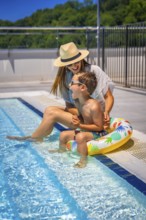 Vertical photo full length of a caucasian mother and kid playing sitting on a swimming pool