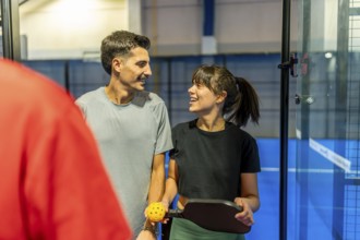 Two smiling adult players holding a paddle and ball, sharing a moment during a friendly pickleball