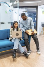 Two young professionals working together, sharing ideas and using a laptop in a modern coworking
