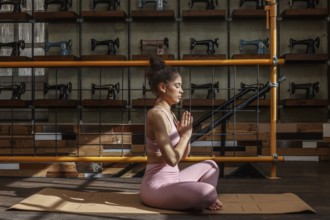 A woman practices yoga meditation in an industrial style room, surrounded by vintage sewing
