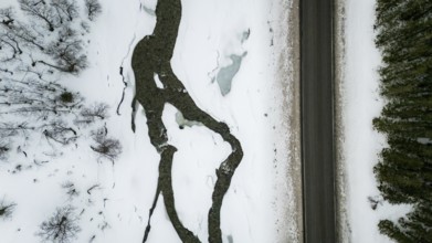 Aerial view of a Nordic landscape showcasing a road flanked by a frozen stream and snow-laden trees