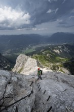 Mountaineer with helmet climbing on the rock in a secured climb, on a narrow rocky ridge, in steep