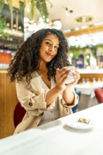 Vertical portrait of a latin beauty woman enjoying warm coffee sitting in a modern cafeteria