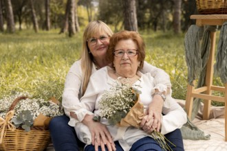 An affectionate mother and daughter pair sit in an idyllic grassy field, surrounded by nature's