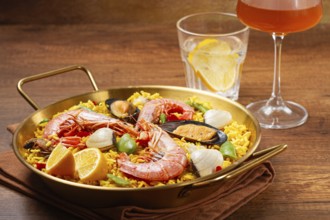 A large dish of seafood paella features shrimp, mussels, and other ingredients. A glass with a