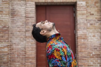 A fashionable cuban man wearing a colorful tropical shirt leans back with his head tilted and