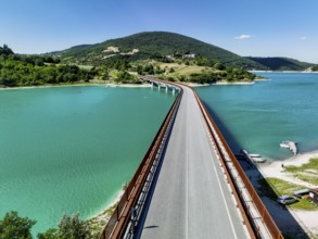 A breathtaking view of a bridge extending over a turquoise lake surrounded by lush hills in Italy,