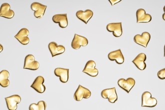 Numerous golden heart shapes artistically arranged on a plain white surface, symbolizing love and