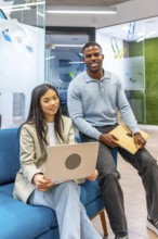 Two smiling business people holding a laptop and a tablet in a modern coworking office, showcasing
