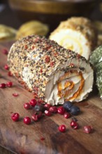 Close-up image of a spiced cheese roll coated with mixed herbs and peppercorns, accented with