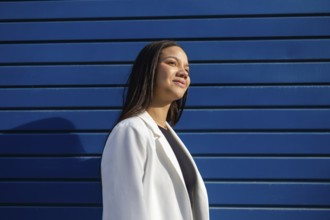 A confident businesswoman in a white blazer smiles against a vibrant blue background. Her