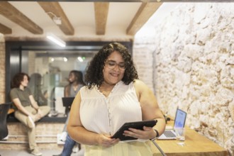 Multiracial coworkers collaborate in a modern office. A woman uses a tablet while others engage in