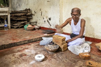 Man sitting smiling in a workshop with bricks and braziers, a man burning sapphires in a small oven