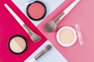 Aesthetic arrangement of makeup brushes and powder compacts on contrasting red, pink and blue