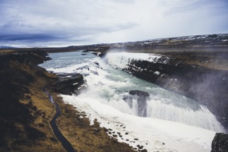 Stunning view of Gullfoss waterfall, cascading powerfully over rugged cliffs. The icy landscape and