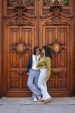 A lesbian couple smiling and embracing in front of an ornate wooden door, exuding love and
