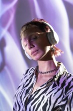 A young, trendy woman wearing headphones enjoys music. Her stylish zebra-print shirt and modern